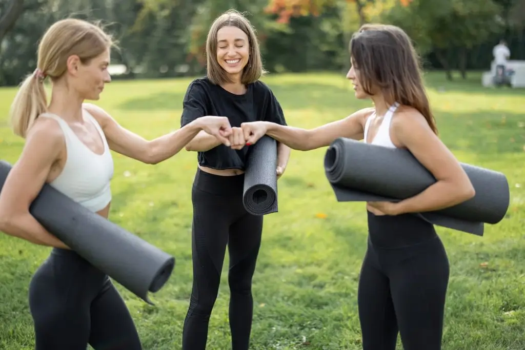 girls-with-fitness-mats-bumping-fists-on-meadow